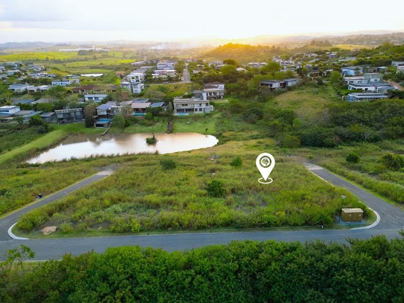 Aerial view of a vacant residential plot featuring road access and proximity to a scenic pond within a developed estate.