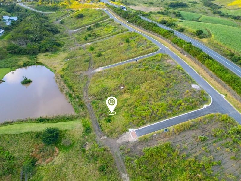 Aerial view of a vacant residential plot featuring natural landscape, proximity to a pond, and established paved road access within the estate.