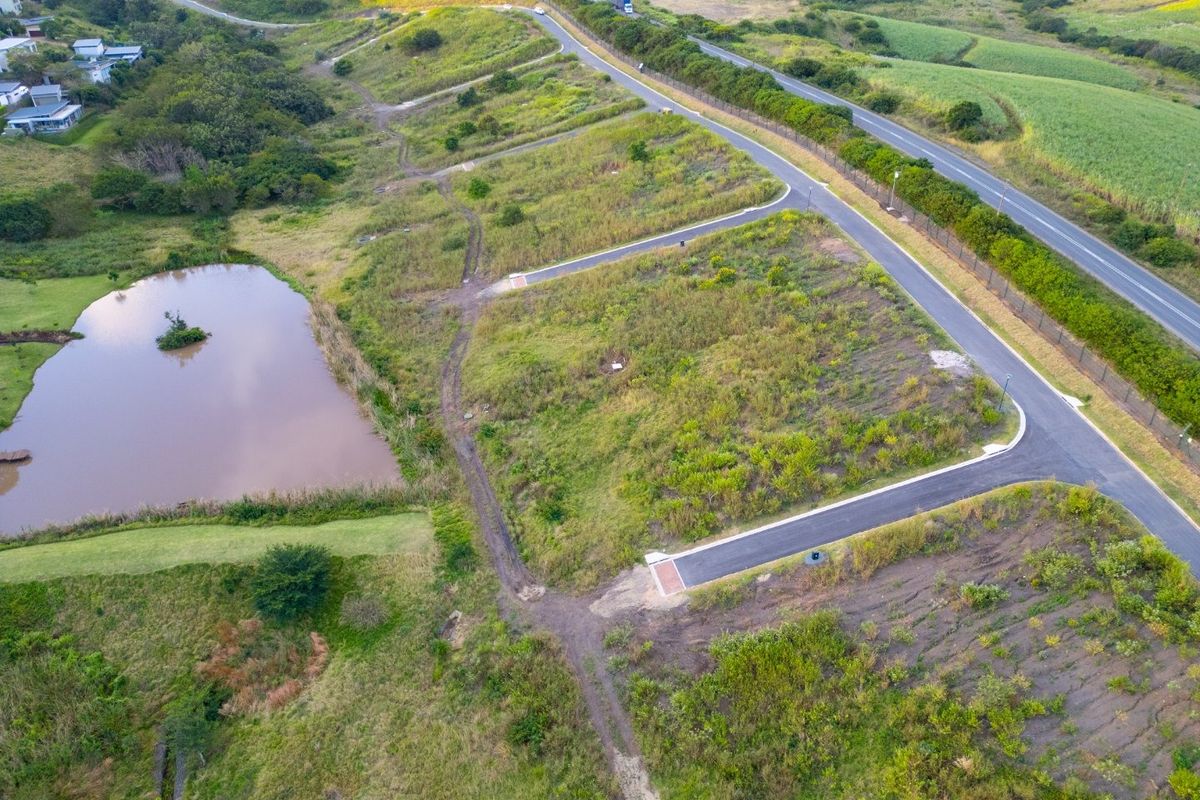 Aerial view of a vacant residential plot featuring established paved road access and proximity to a natural pond within a landscaped estate.