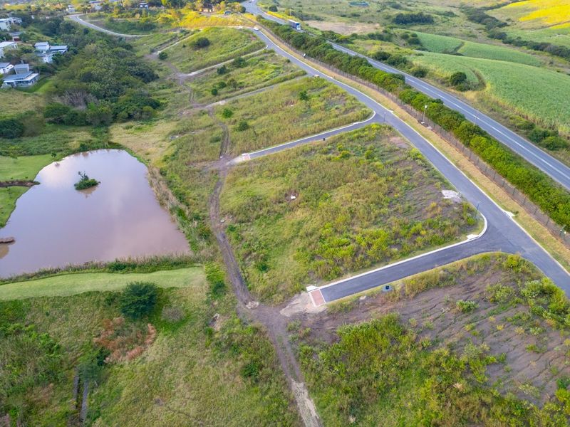 Aerial view of a vacant residential plot featuring established paved road access and proximity to a natural pond within a landscaped estate.
