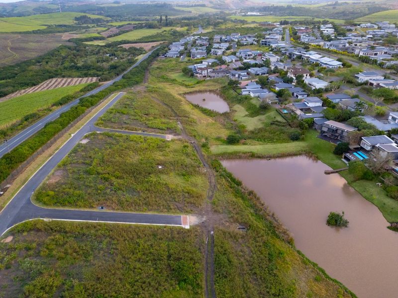 Aerial view of a vacant residential land plot situated within a developed estate, featuring adjacent paved roads and natural retention ponds.