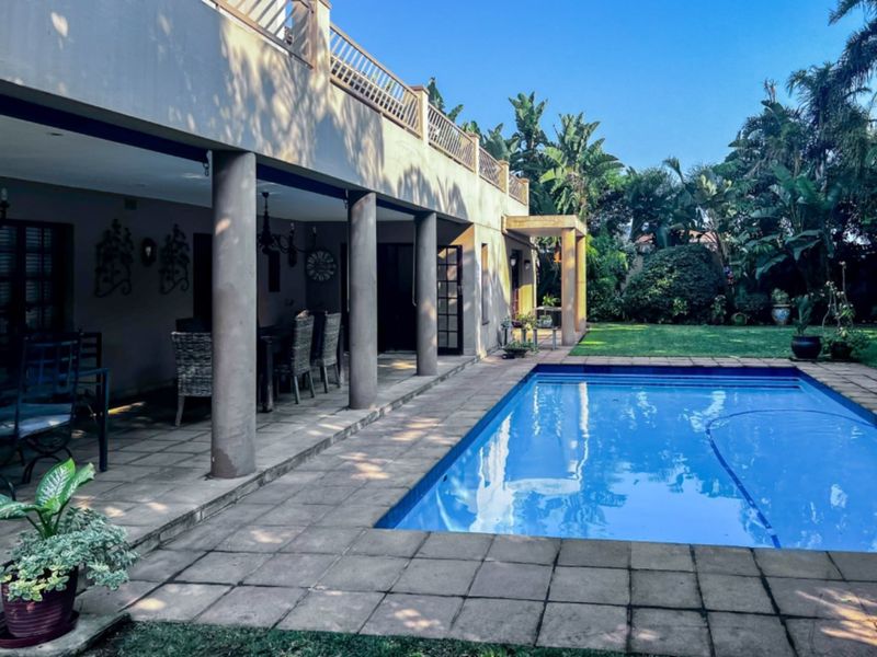 Spacious outdoor entertainment area featuring a swimming pool, paved deck, and a covered patio with structural columns.