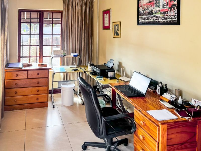 A functional home office space featuring tiled flooring and a large window with natural light, suitable for a dedicated workspace.