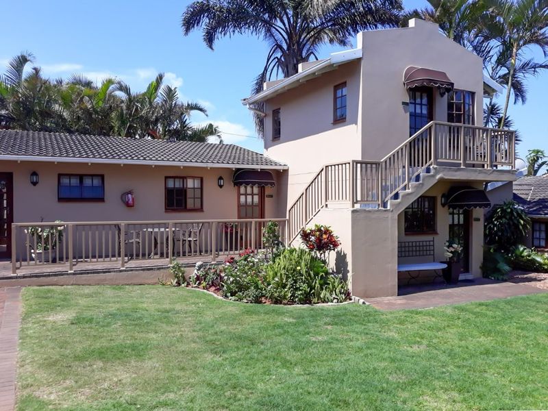 A well-maintained guest house exterior featuring a timber deck, external staircase leading to a balcony, and landscaped garden area.