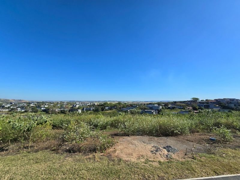 A wide-angle view overlooking a residential neighborhood and surrounding landscape from the vacant land plot.