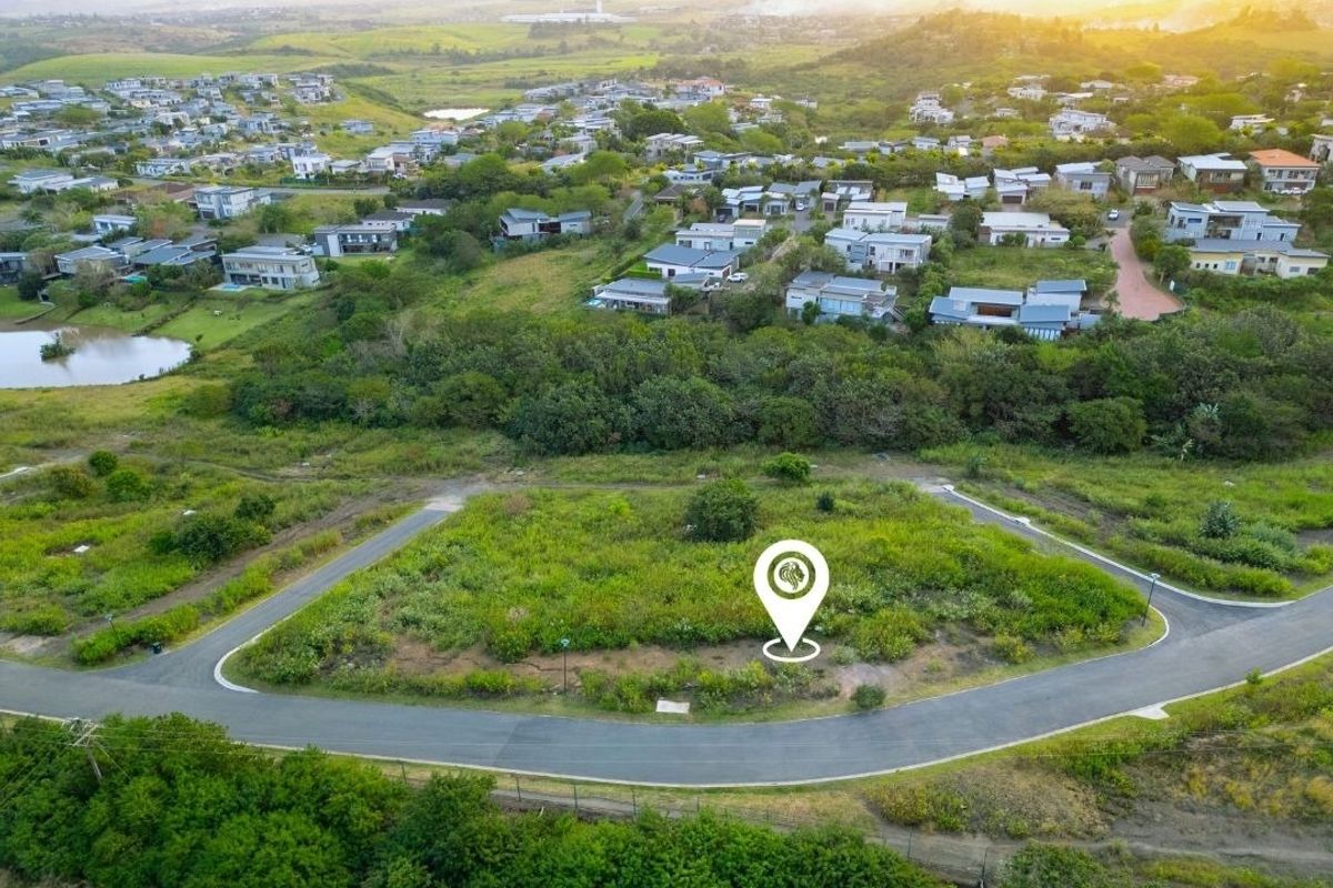 An aerial view of a vacant residential plot situated within a developed estate, featuring paved road access and surrounding landscape.