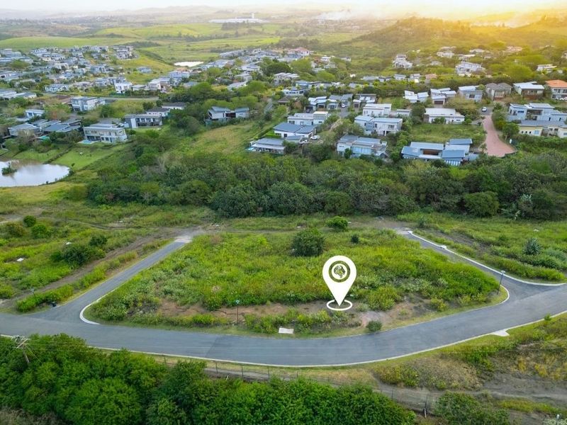 An aerial view of a vacant residential plot situated within a developed estate, featuring paved road access and surrounding landscape.
