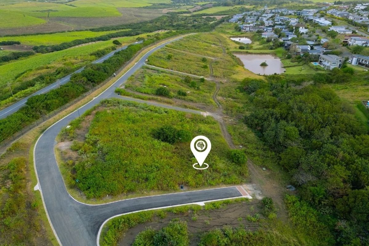 Aerial view of a vacant residential plot featuring established road infrastructure and surrounding green landscape in a developing estate.
