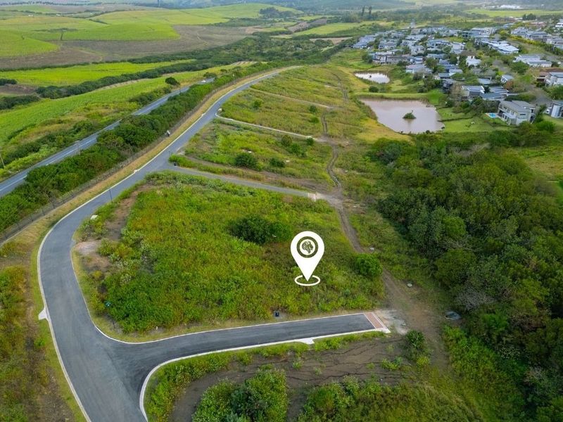 Aerial view of a vacant residential plot featuring established road infrastructure and surrounding green landscape in a developing estate.