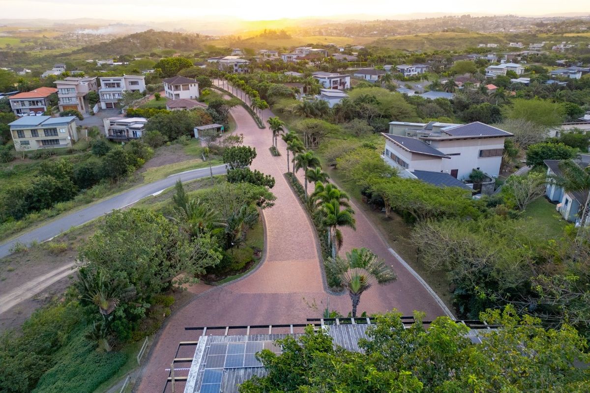 Aerial view of a well-maintained residential estate featuring paved roads, lush landscaping, and surrounding homes at sunset.