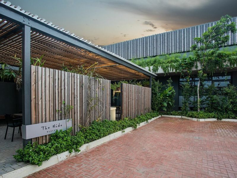 Modern exterior entrance featuring a timber slat pergola, privacy screening, and well-maintained landscaped garden beds with brick paving.