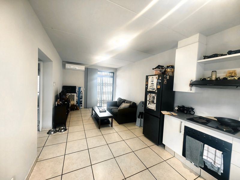 Open-plan living area featuring a functional kitchen with built-in appliances, tiled flooring, and direct access to a balcony through a security gate.