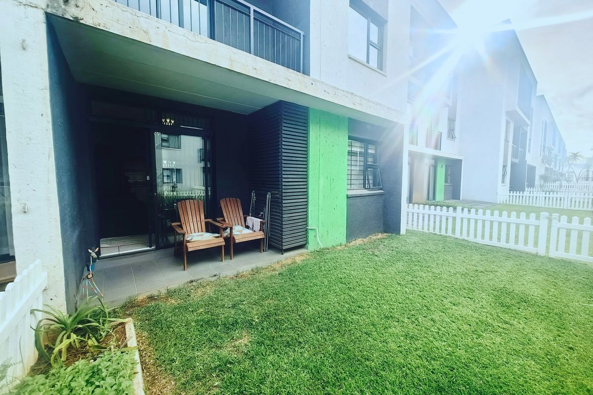 Ground floor apartment featuring a private tiled patio, small garden area with a white picket fence, and an overhead balcony.