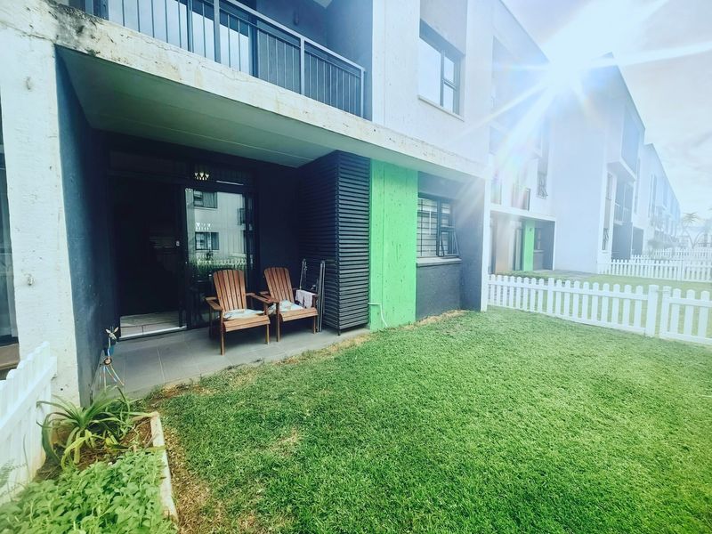 Ground floor apartment featuring a private tiled patio, small garden area with a white picket fence, and an overhead balcony.