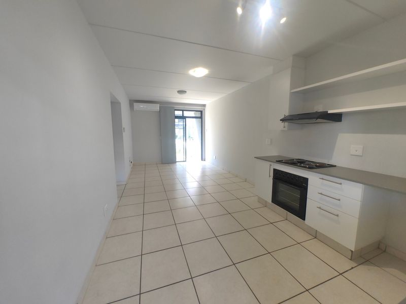 An open-plan living and kitchen area featuring tiled flooring, modern built-in cabinetry, integrated oven and hob, and an air conditioning unit.