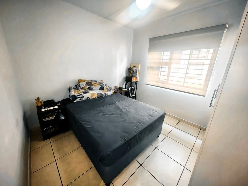 A functional bedroom featuring tiled flooring, a roller blind for privacy, security bars on the window, and a built-in wardrobe.