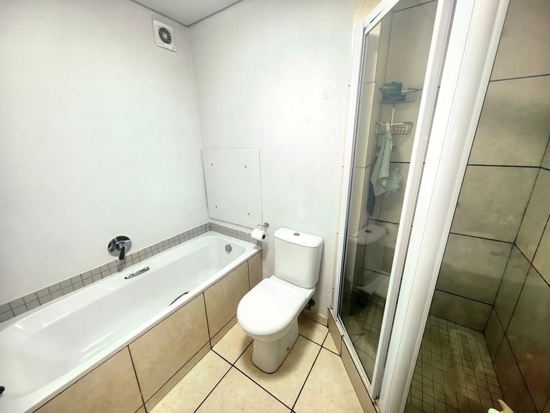A functional bathroom featuring a built-in bathtub, separate shower enclosure, and toilet with neutral tiled finishes.