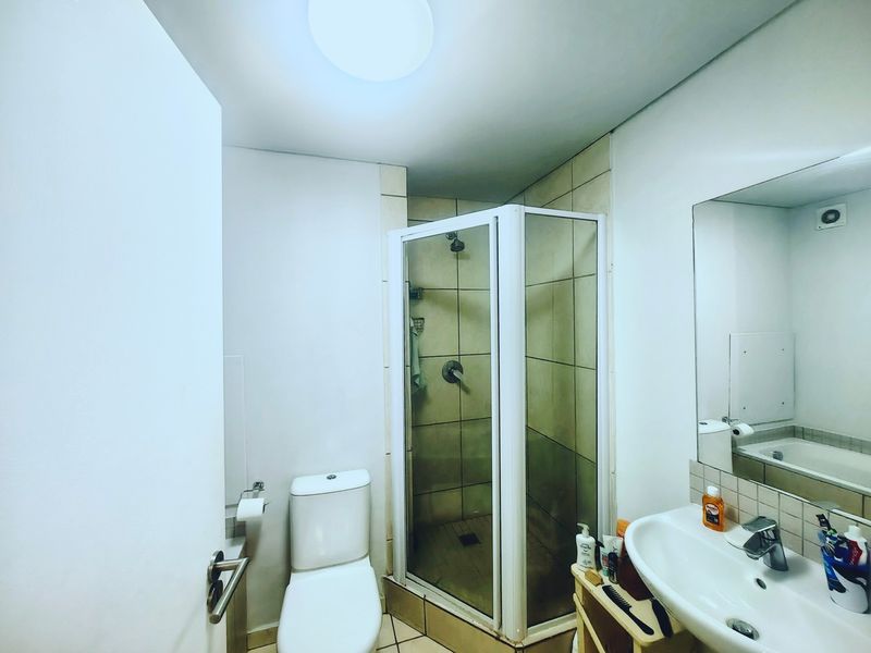 A functional bathroom featuring a shower enclosure, toilet, and wall-mounted basin with a large mirror.