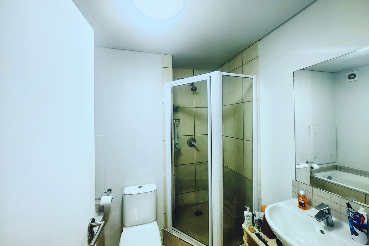A functional bathroom featuring a shower enclosure, toilet, and wall-mounted basin with a large mirror.