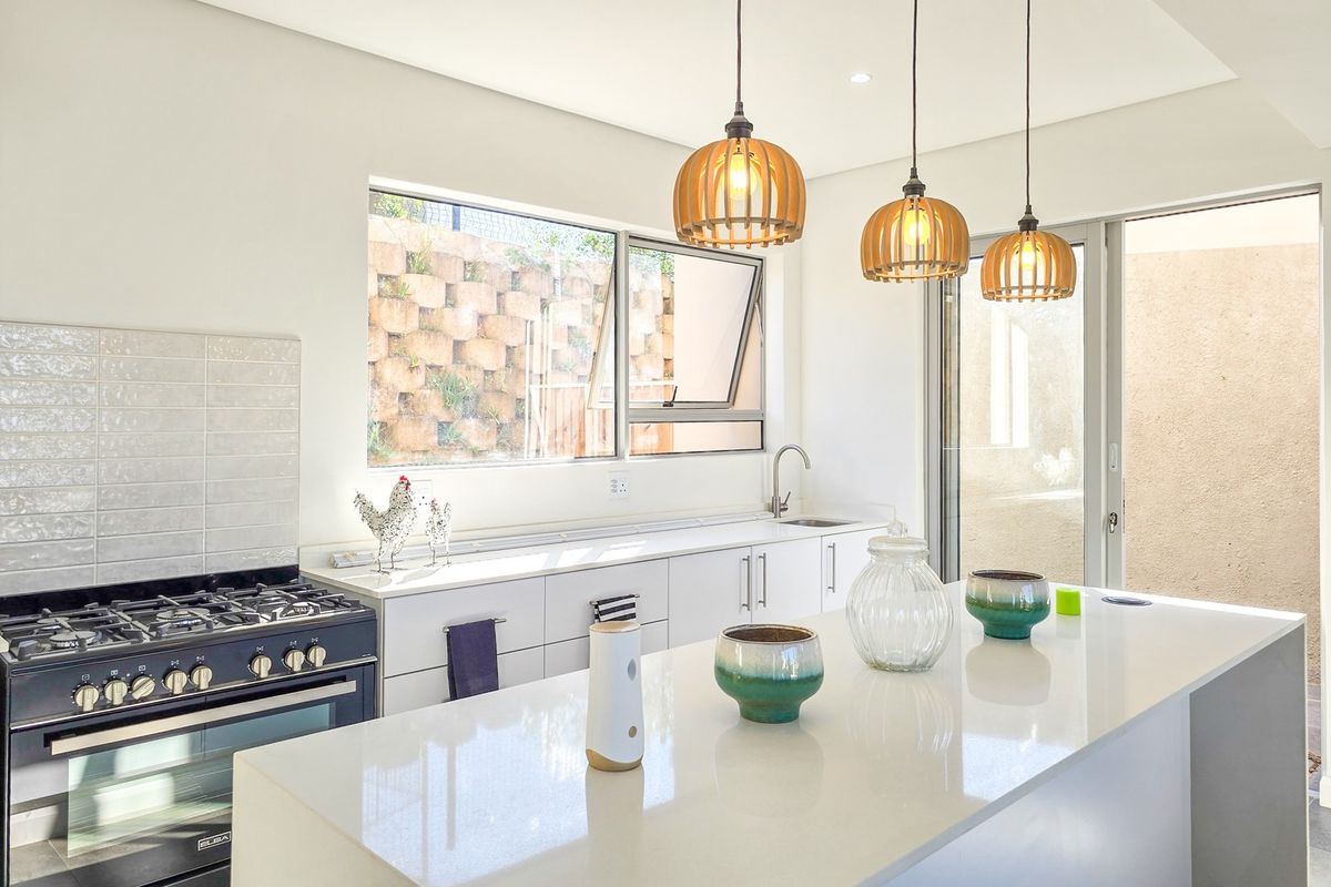 Modern kitchen featuring a large island with quartz countertops, gas stove, sleek cabinetry, and pendant lighting, with direct access to an outdoor area.