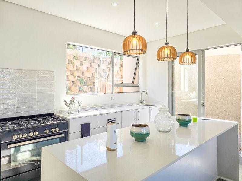 Modern kitchen featuring a large island with quartz countertops, gas stove, sleek cabinetry, and pendant lighting, with direct access to an outdoor area.