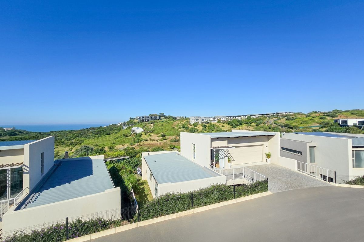 Aerial view of modern residential properties featuring paved driveways, garages, and metal roofing, set within a coastal landscape.