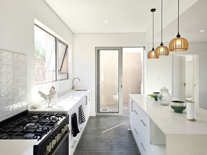 Modern kitchen featuring a central island, quartz countertops, gas stove, and sleek cabinetry with contemporary pendant lighting and direct access to an outdoor area.