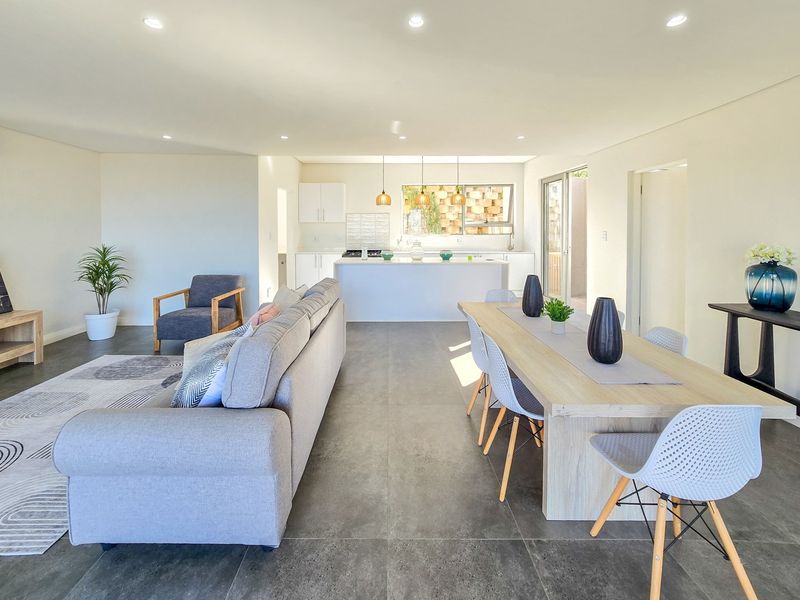 Spacious open-plan living and dining area featuring a modern kitchen with a central island, tiled floors, and abundant natural light through sliding glass doors.