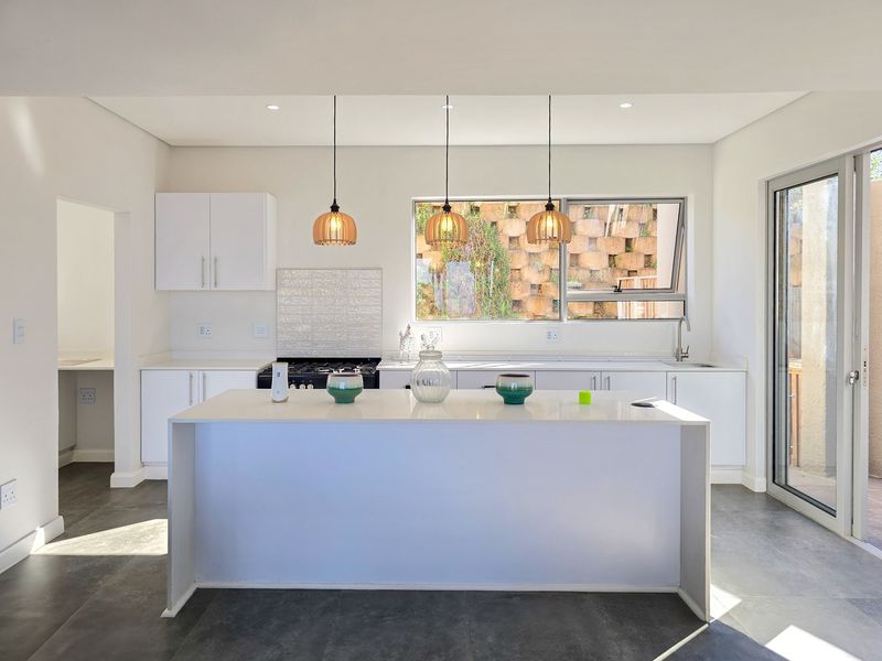 Modern kitchen featuring a central island, white cabinetry, gas stove, tiled backsplash, and direct access to the outdoor area through a sliding glass door.