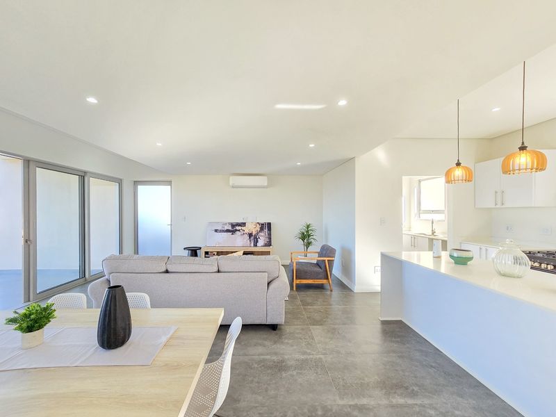 Modern open-plan living area featuring a sleek kitchen with island, tiled floors, recessed lighting, and seamless access to the outdoor patio through sliding doors.