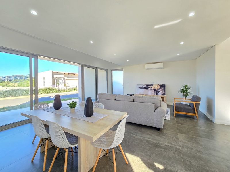 Bright open-plan living and dining area featuring large format floor tiles, recessed lighting, and expansive sliding glass doors leading to the exterior.