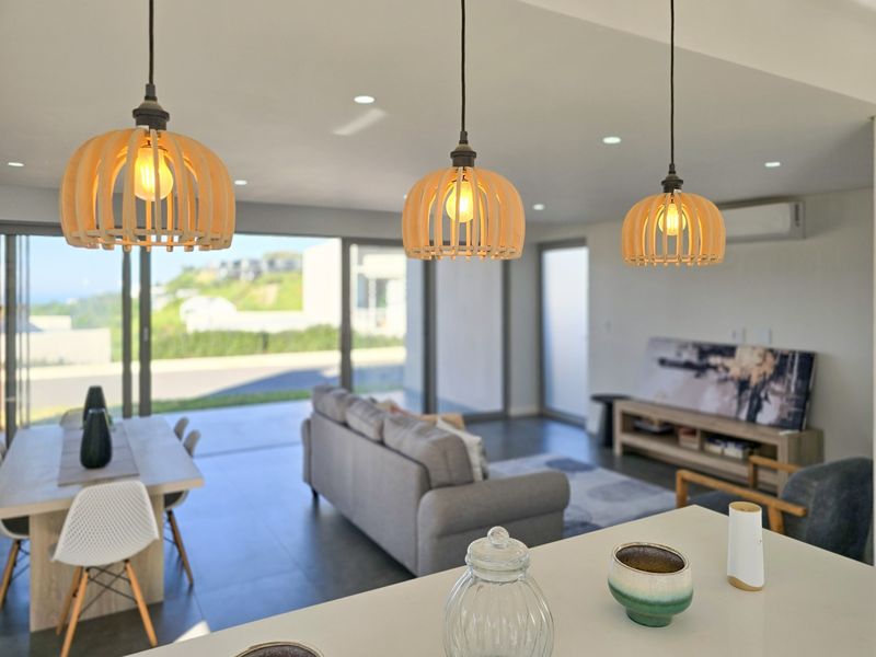 Modern open-plan living area featuring tiled floors, recessed lighting, stylish pendant fixtures, and large sliding glass doors leading to an outdoor space.