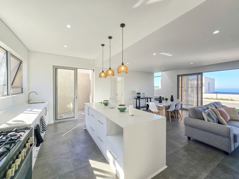 Modern open-plan living area featuring a sleek kitchen with a central island, gas stove, and seamless flow to the outdoor patio and ocean views.