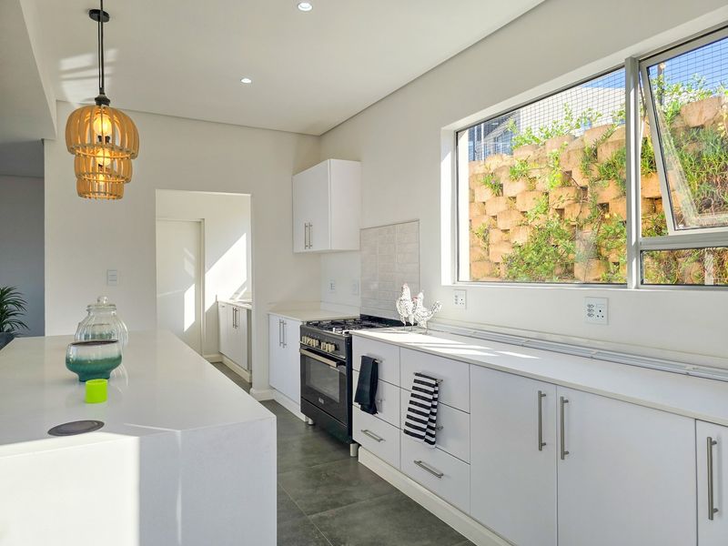 Modern kitchen featuring a central island, white cabinetry, stone countertops, gas stove, and large window overlooking a landscaped retaining wall.