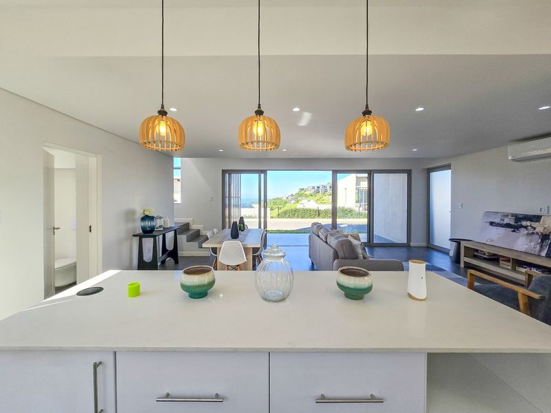 Modern open-plan living area featuring a sleek kitchen island, contemporary pendant lighting, and seamless flow to an outdoor patio with scenic views.