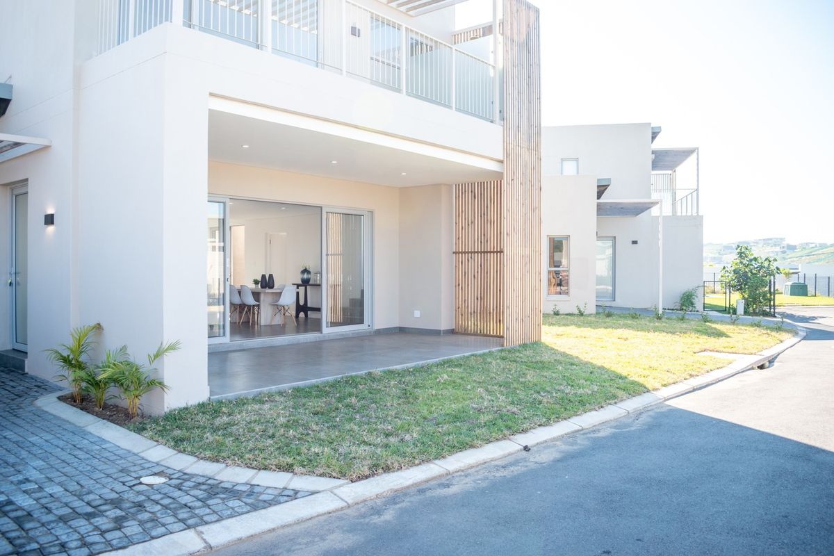 Modern residential exterior featuring a covered ground-floor patio with sliding doors, an upper-level balcony, and contemporary timber slat architectural detailing.