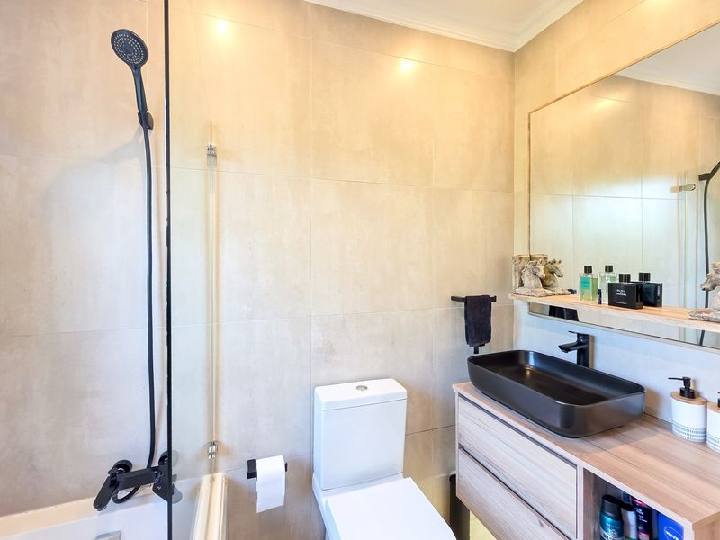 Modern bathroom featuring a neutral tiled wall, a sleek black vessel sink on a wood-finish vanity, and a combined shower and bathtub setup.
