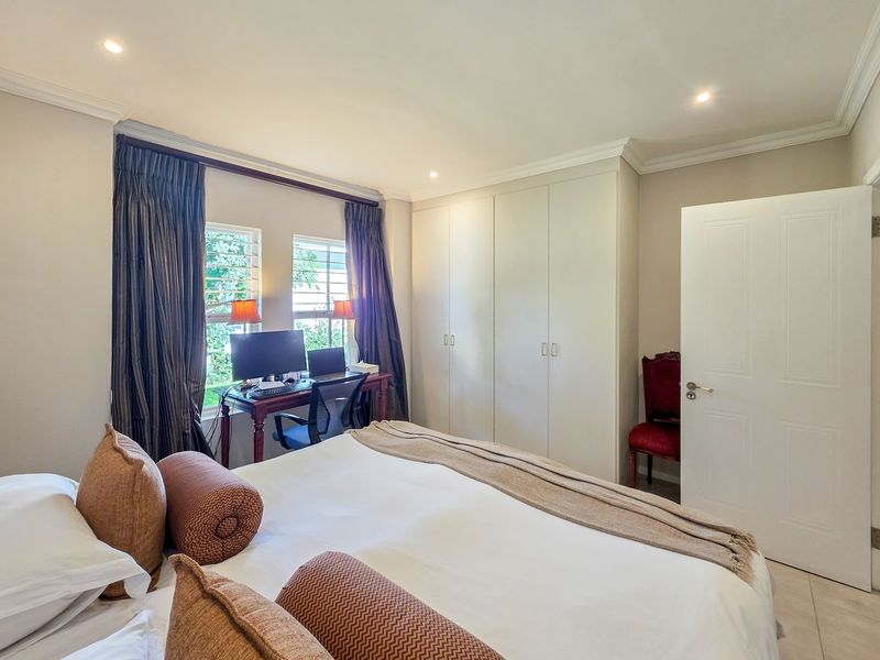 A well-maintained bedroom featuring built-in cupboards, recessed downlighting, and neutral tiled flooring, offering a clean and functional living space.