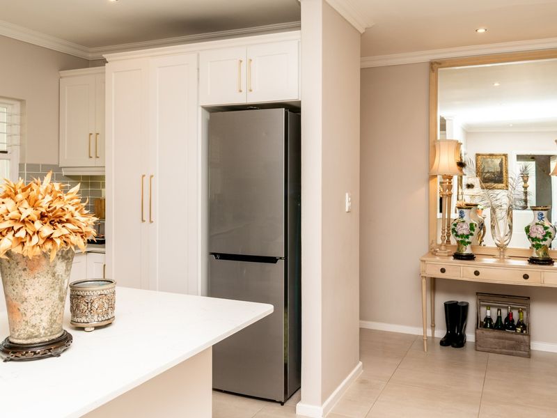 A modern, well-maintained kitchen featuring white cabinetry, stone countertops, and a subway tile backsplash, seamlessly transitioning into an adjacent hallway area.