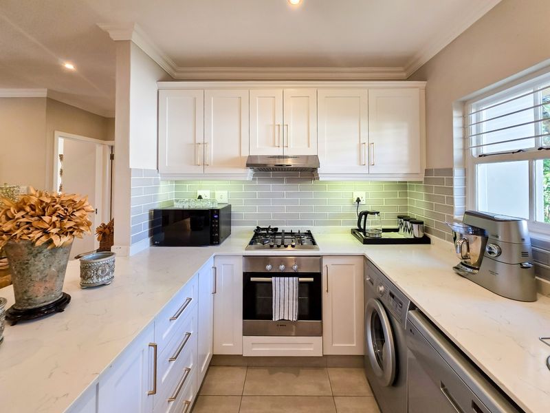 Modern kitchen featuring white cabinetry, quartz countertops, subway tile backsplash, and integrated appliances including a gas hob, oven, and laundry facilities.