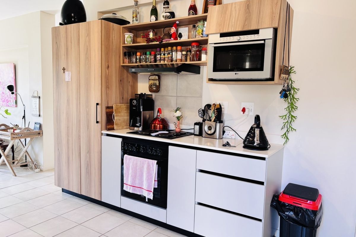 A modern kitchen featuring light wood-grain cabinetry, white stone countertops, built-in oven, hob, and integrated microwave with tiled flooring.
