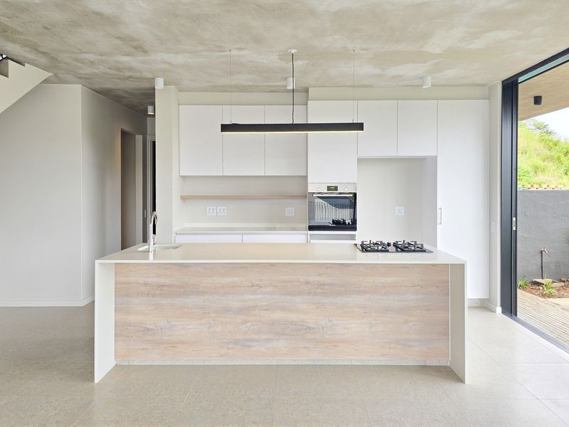 Modern open-plan kitchen featuring a central island with a gas hob and sink, sleek white cabinetry, and a raw concrete ceiling finish.
