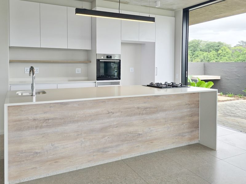 Modern kitchen featuring a large island with quartz countertops, built-in oven, gas hob, and seamless handleless cabinetry, opening directly to an outdoor patio area.