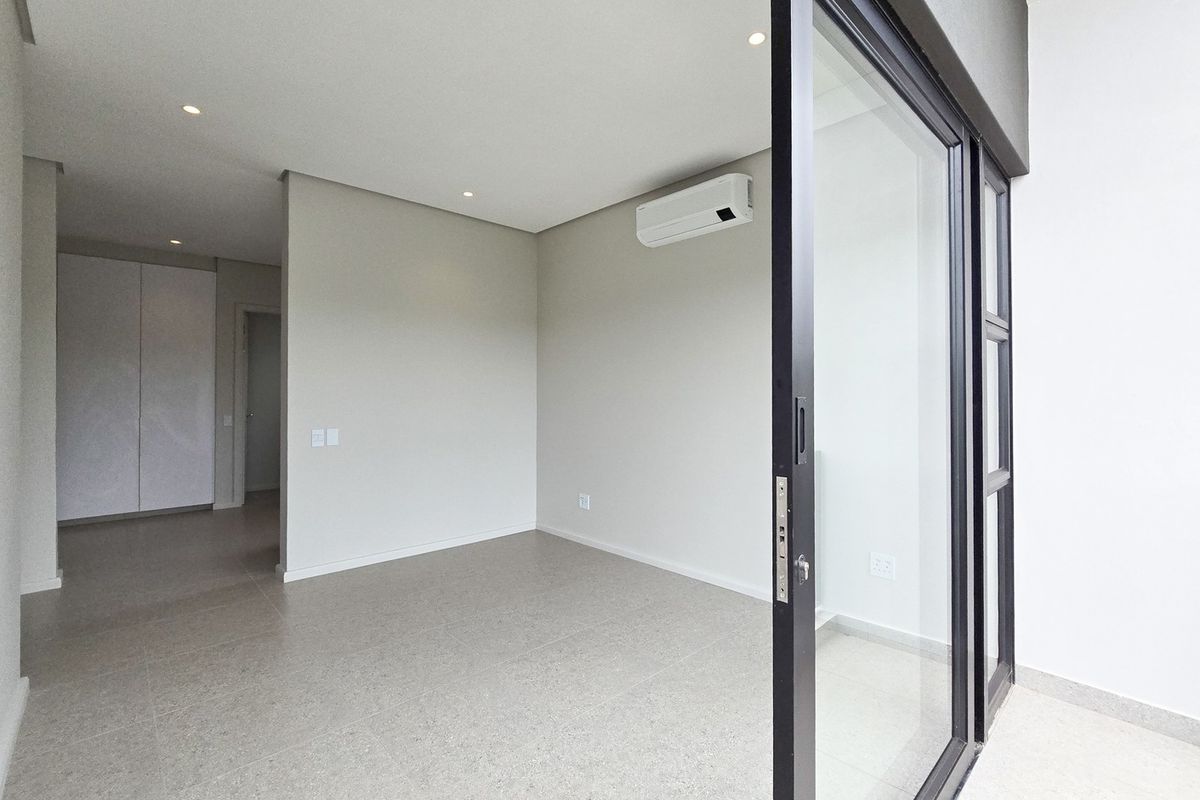 A bright, modern, and empty living area featuring neutral tiled flooring, recessed lighting, a split-system air conditioner, and large sliding glass doors.