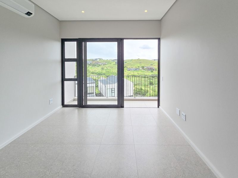 A bright, modern, and empty bedroom featuring tiled floors, recessed lighting, a split-system air conditioner, and a sliding door leading to a balcony.