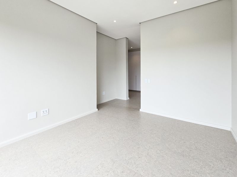 A bright, modern, and empty bedroom featuring neutral tiled flooring, recessed downlighting, and built-in storage cupboards.