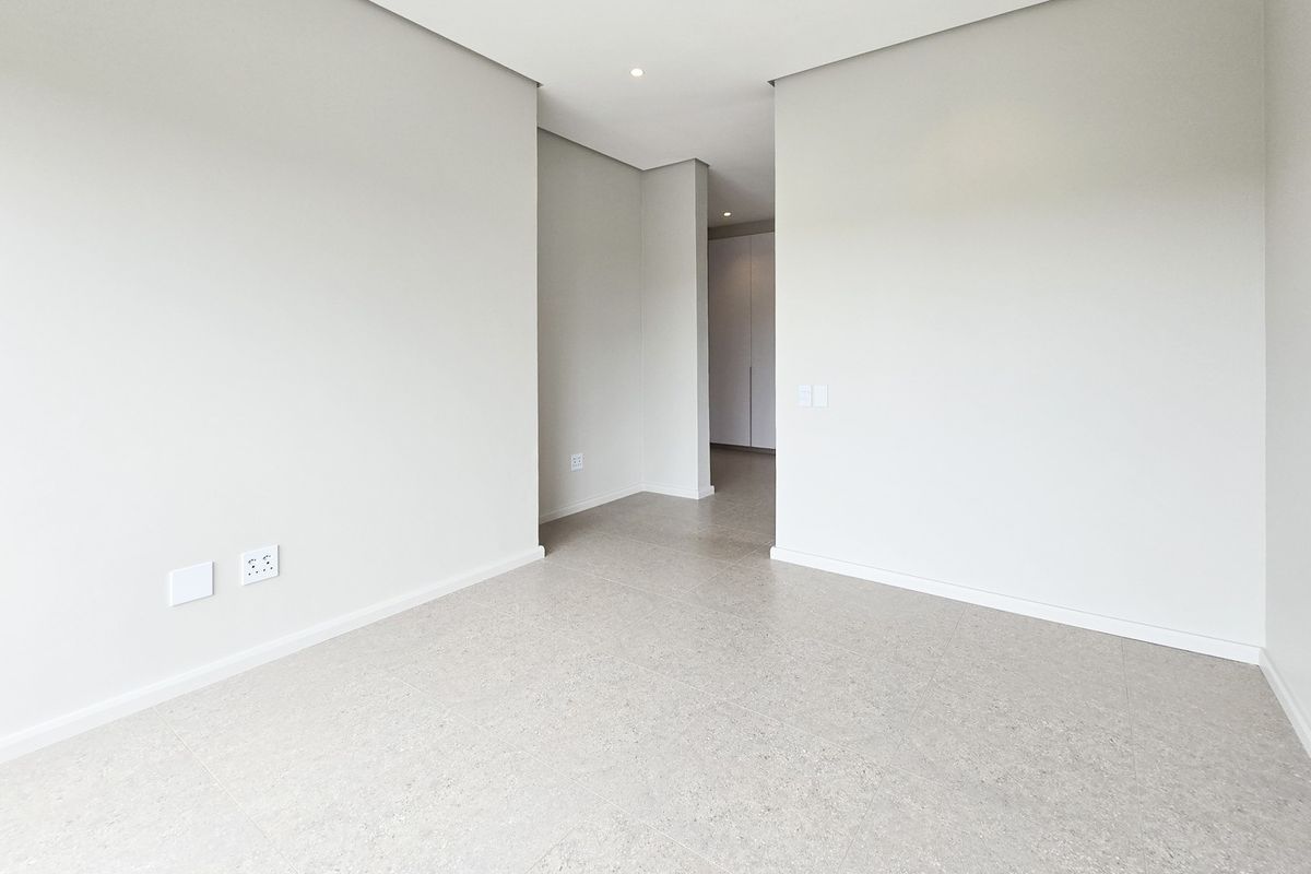 A bright, modern, and empty bedroom featuring neutral tiled flooring, recessed downlighting, and built-in storage cupboards.