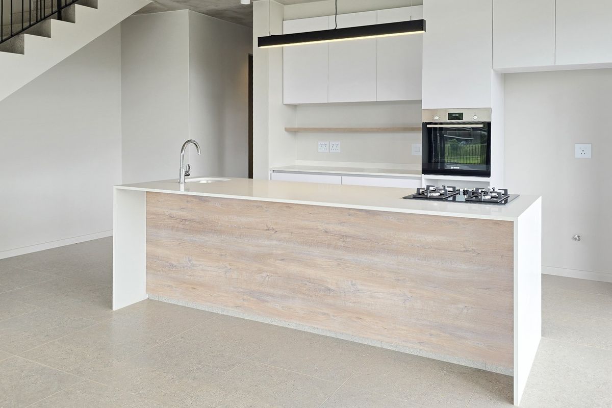 Modern open-plan kitchen featuring a central island with stone countertops, built-in oven, gas cooktop, and sleek cabinetry, adjacent to an architectural staircase.