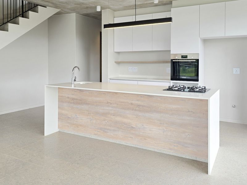 Modern open-plan kitchen featuring a central island with stone countertops, built-in oven, gas cooktop, and sleek cabinetry, adjacent to an architectural staircase.