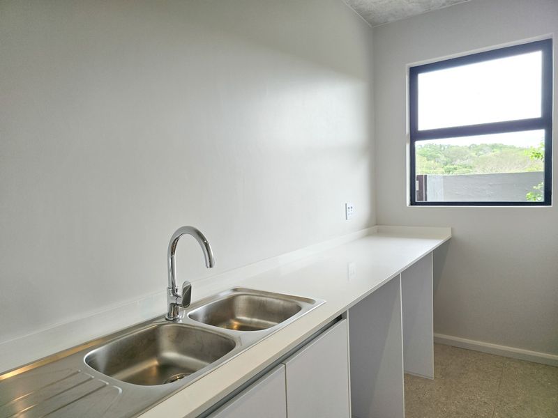 A clean, modern laundry area featuring a double stainless steel sink, stone countertop, and ample under-counter space for appliances.